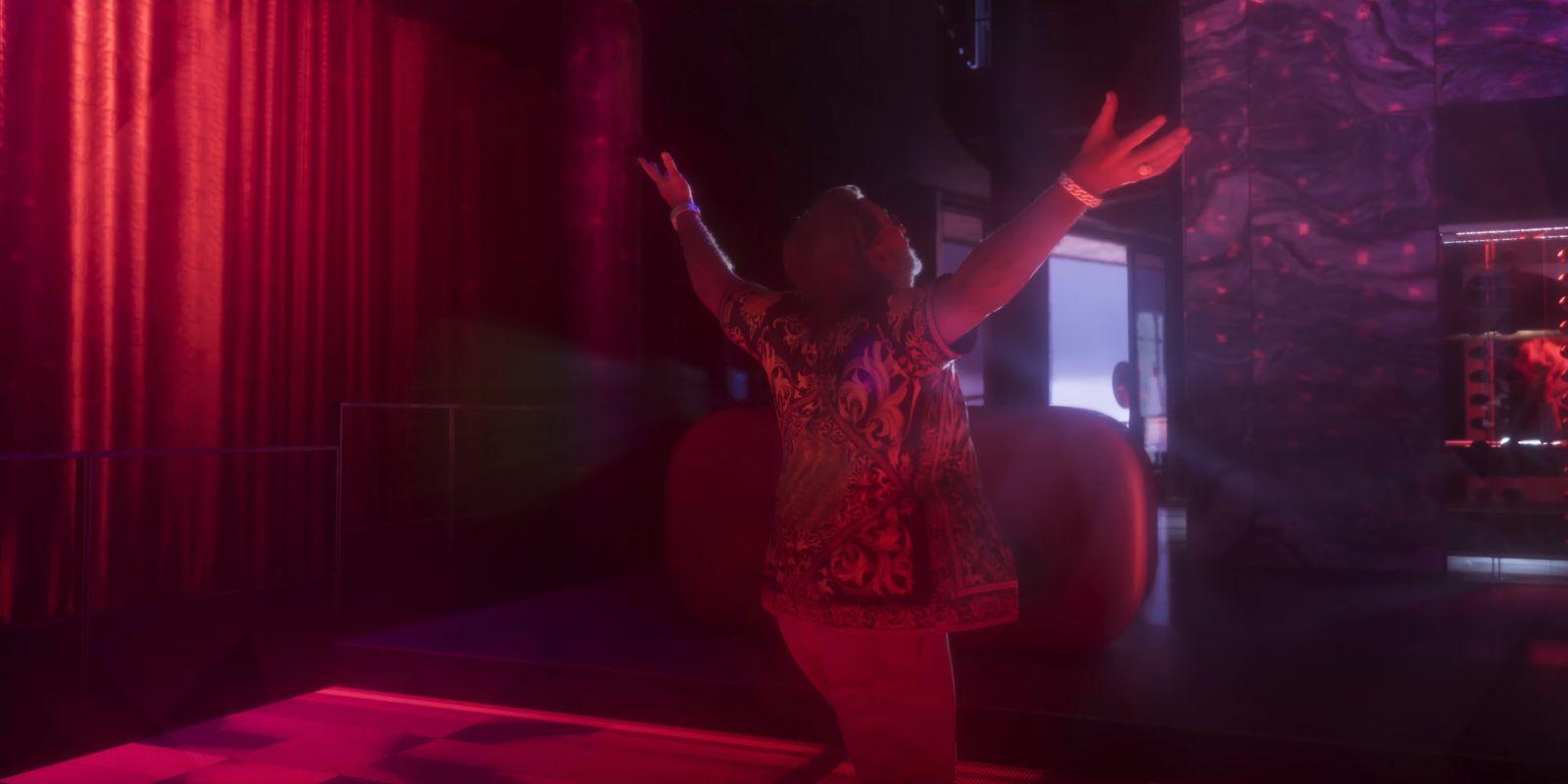 A man spreads his arms beneath red and purple club lights.