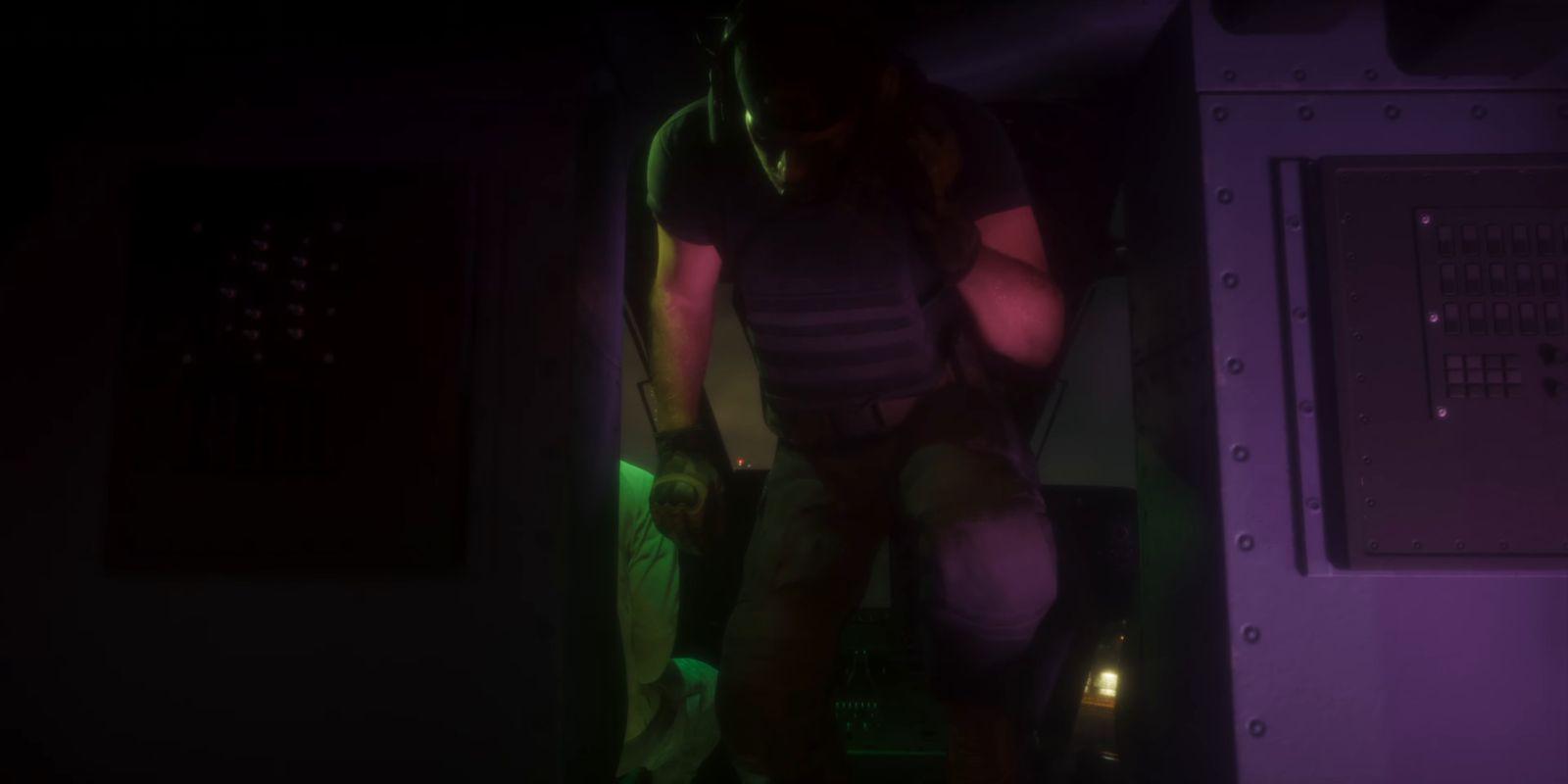 An armed man in body armour moves through a dark doorway.