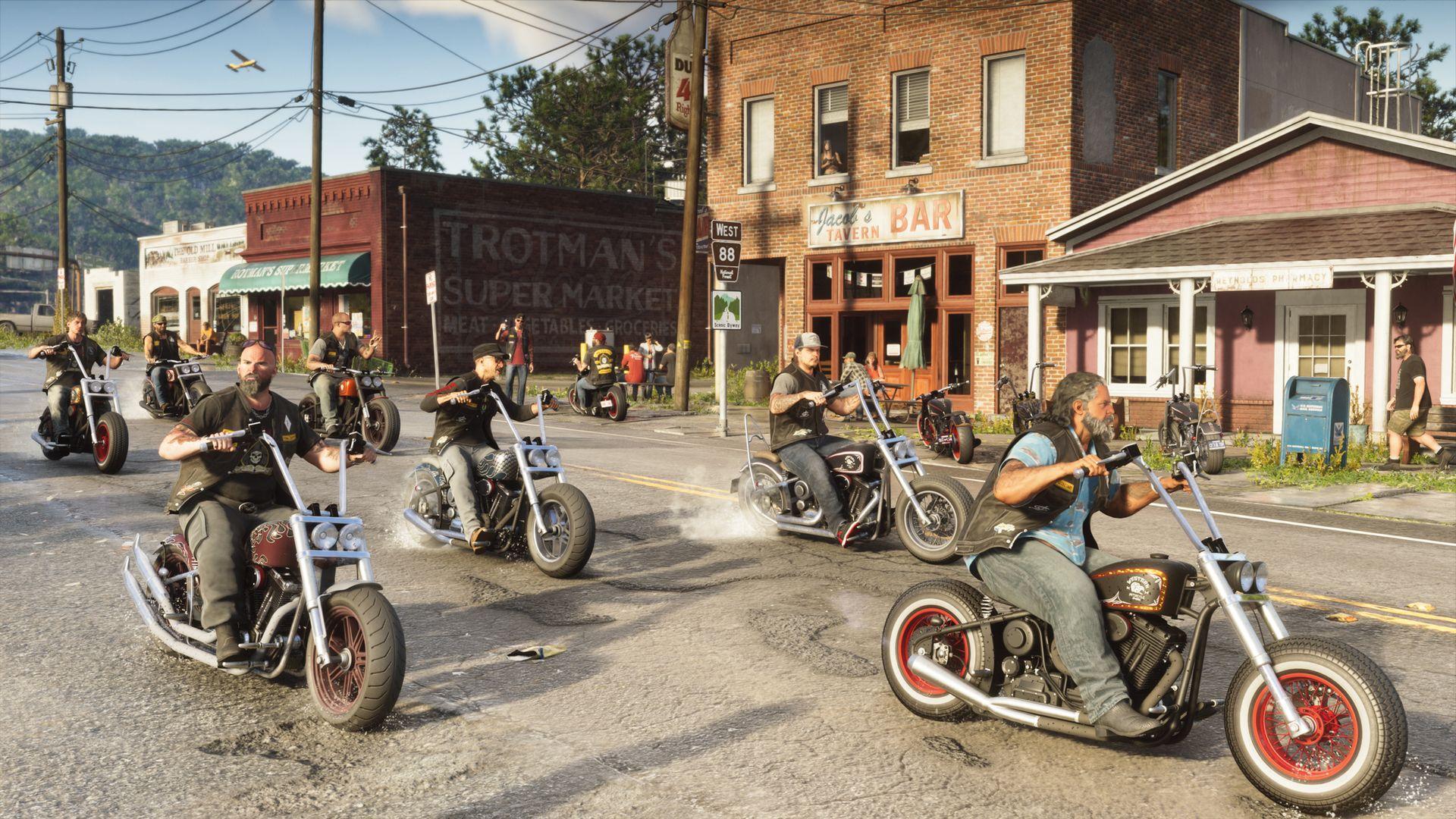 A group of motorcyclists rides past shops and a bar on a town street.