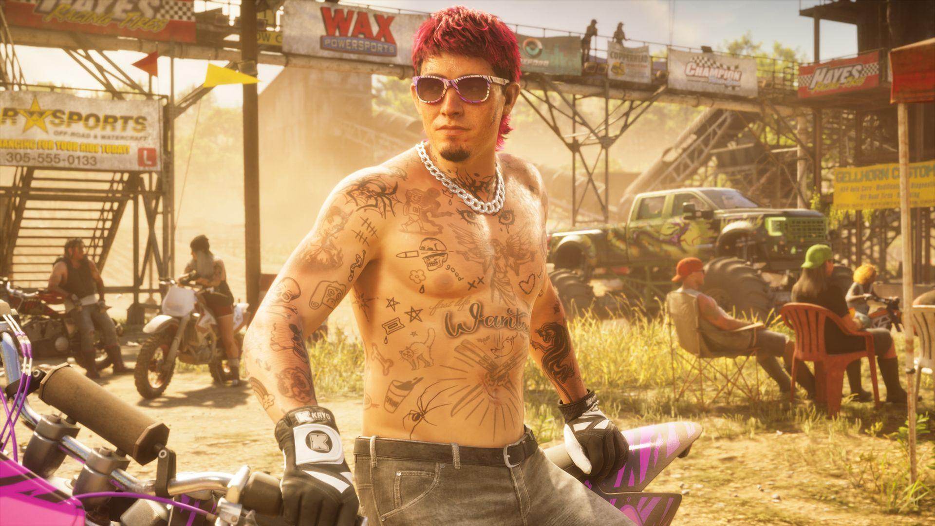 A red-haired, tattooed man stands beside a motorcycle at an outdoor gathering.