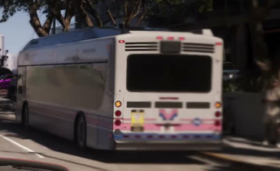 Rear three-quarter view of a white coach with pink and blue graphics parked beside a street.